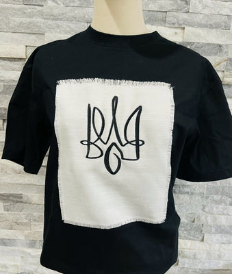 Black T-shirt with an embroidered Tryzub (Ukrainian trident) design on a white textured patch. Minimalistic, stylish, and patriotic